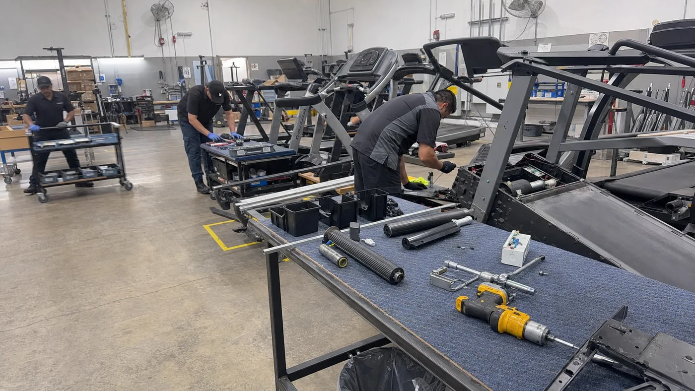 Technicians working on treadmill components at repair benches